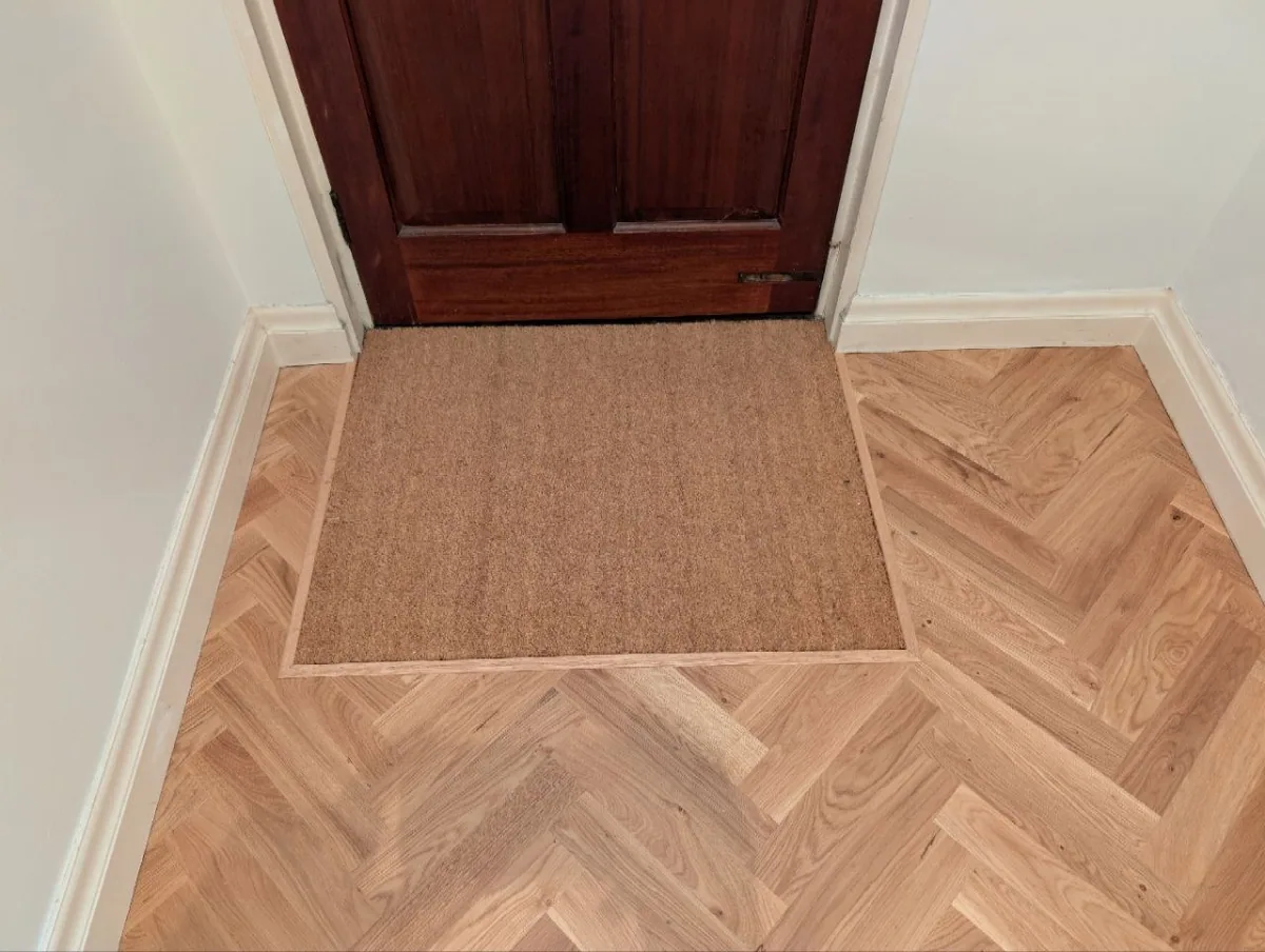 Coir doormat cut flush into an oak herringbone floor at a front door in Waterloo